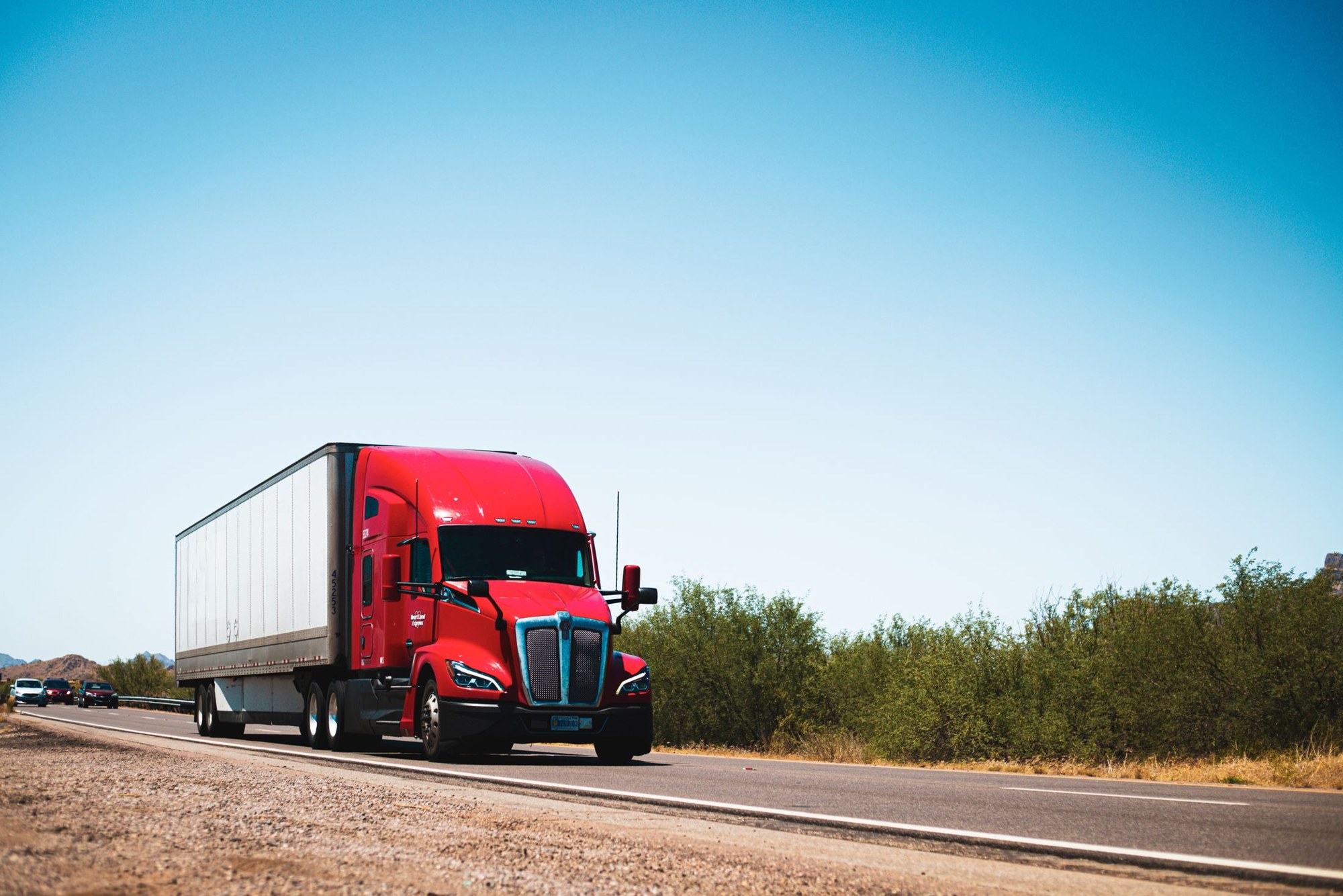 Red American semi truck hauling a white trailer along a rural highway